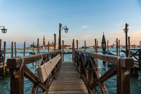 Wooden pier with gondolas and lamps leading to san giorgio maggiore in venice at sunset, creating a