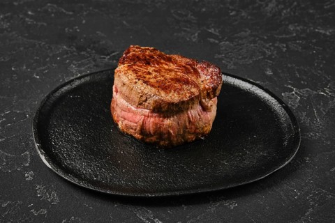 Perfectly seared filet mignon sits on a dark plate, highlighting its rich color and inviting look.