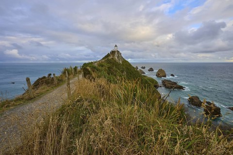 Path leading to a lighthouse on a cliff overlooking the sea under a cloudy sky, summer, Nugget