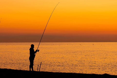 A man fishing just in front of sunrise on the Costa Rei, a coastline of the Italian island of