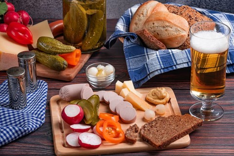 Rustic snack with sausage, cheese, beer, mustard, radishes and bread on a laid table