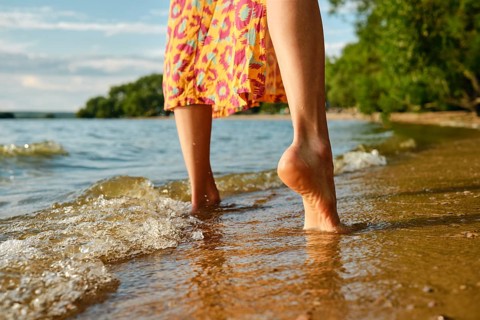 Low angle rear view of bare female feet on a calm beach. The gentle waves lap female feet