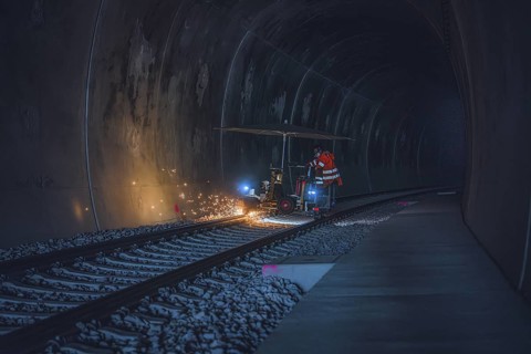 A worker in an orange waistcoat works on the rails in a dark tunnel while sparks fly, grinding work