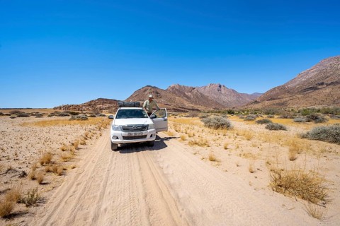 Young man standing in the open door of an off-road vehicle, sandy track, desert landscape with