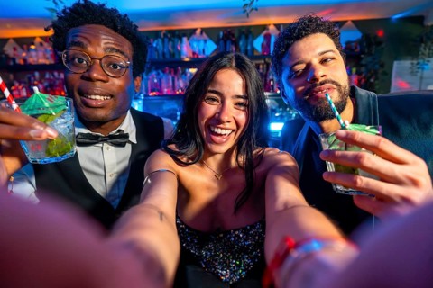 Cheerful friends capturing a joyful selfie while savoring colorful cocktails in a lively nightclub