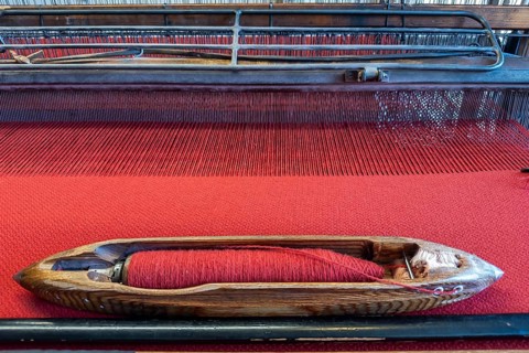 Old loom in the clothmaking museum in Bramsche, Lower Saxony, Germany, wooden shuttle on red fabric