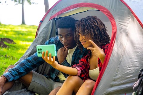 Two young campers are taking a selfie inside their tent, enjoying a moment of fun during their