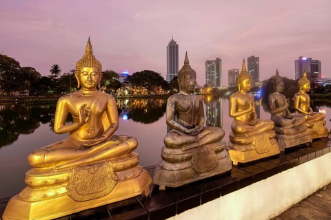 Buddha statues of Seema Malaka Temple at Beira Lake at sunset, Colombo skyline behind, Sri Lanka