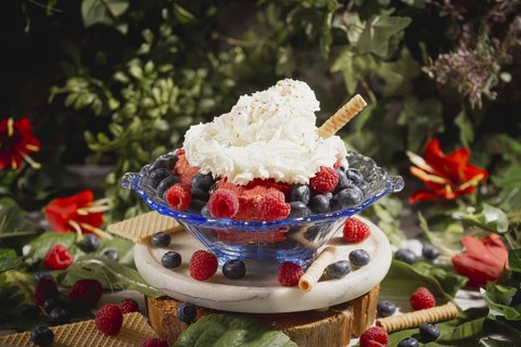 Ice cream sundae with raspberries and blueberries, decorated with cream and a wafer stick,