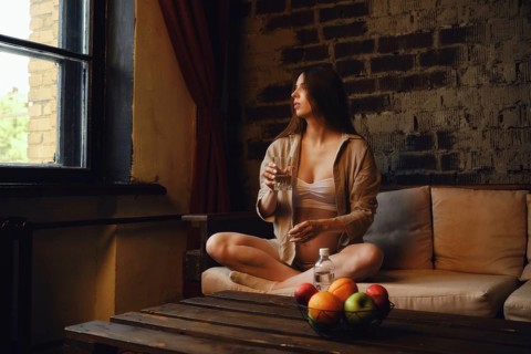 In a cozy home setting, a pregnant woman sits comfortably on a couch with a glass of mineral water,