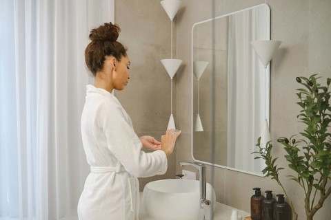 A young woman wearing a white bathrobe stands at a sleek sink in a stylish bathroom