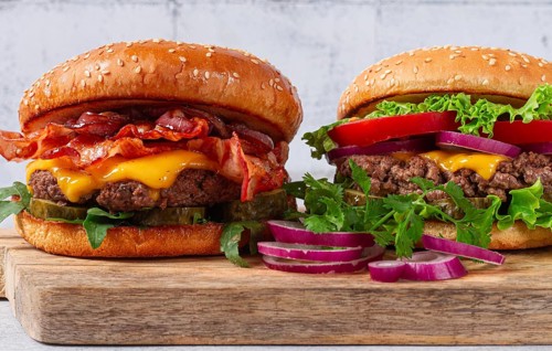 Two burgers with beef patty, fried bacon, cheddar cheese, tomatoes, on a light table