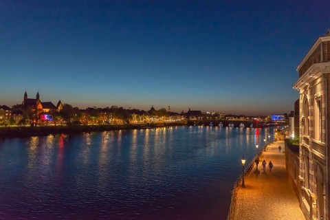 Maastricht, Netherlands, night view of the river Maas with illuminated bridge and promenade, under