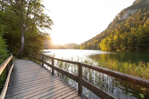 Sunrise in summer at Lake Thumsee near Bad Reichenhall with a wooden footbridge and a sun star over