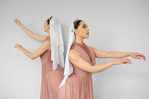 Two ballerinas standing back to back and waving hands on grey background