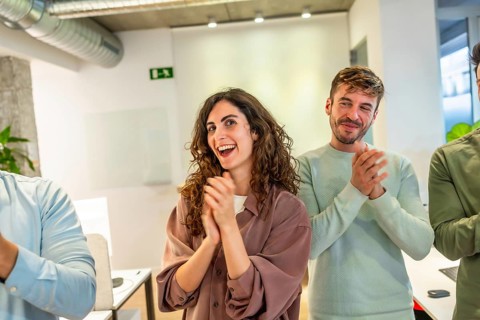 Group of smiling businesspeople applauding during a meeting in a modern office, celebrating success