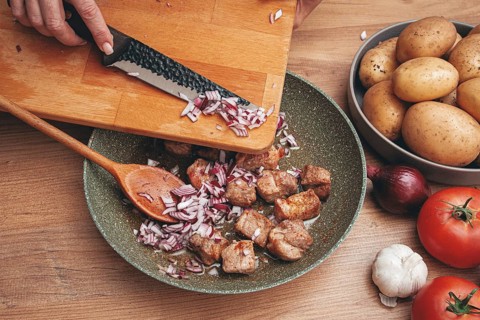 Adding chopped onion to the pan with meat, close-up