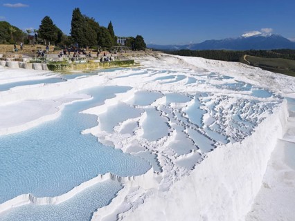 View of limestone terraces with turquoise blue water surrounded by trees and tourists, aerial view,