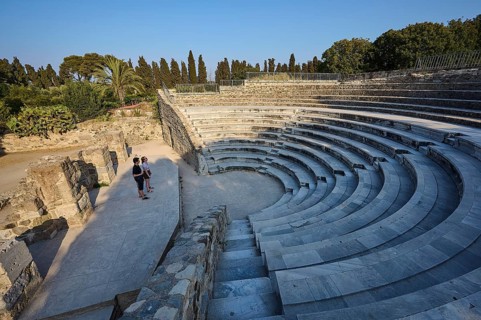 Ancient amphitheatre with stone steps and a few visitors, surrounded by nature, Ancient Theatre,