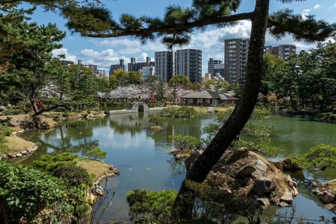 Shukkei-en with Sekisui-gan stone formation, green plants, trees and Koko-kyo stone bridge over