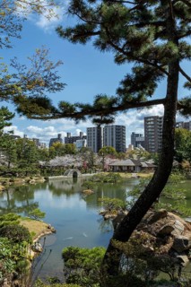 Shukkei-en with Sekisui-gan stone formation, green plants, trees and Koko-kyo stone bridge over