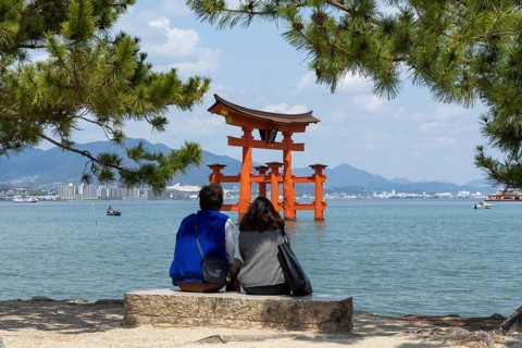 A couple on the beach looking at the torii in the water, landmark, tourist attraction, UNESCO World
