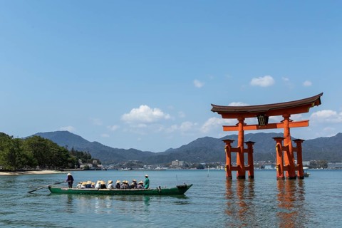 An excursion boat with tourists passes through the torii in the water, sight, tourist attraction,