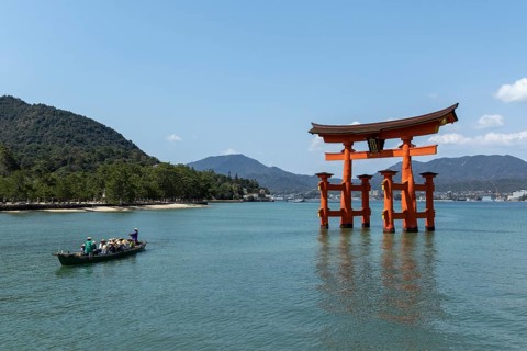 An excursion boat with tourists passes through the torii in the water, sight, tourist attraction,
