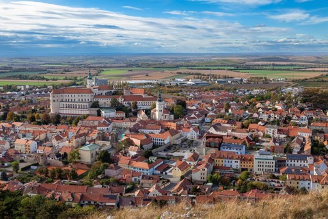 Panoramic view of a town with a historic castle and churches, surrounded by fields and clouds,