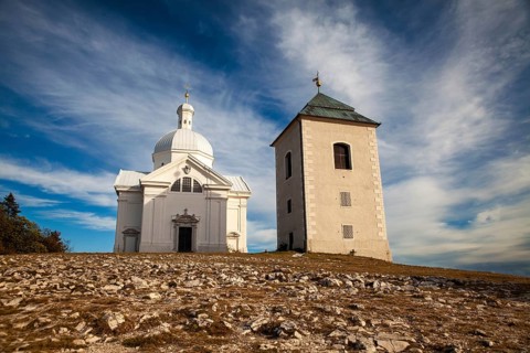 White church and tower in an open landscape under a blue sky with clouds, Mikulov Nikolsburg Czech