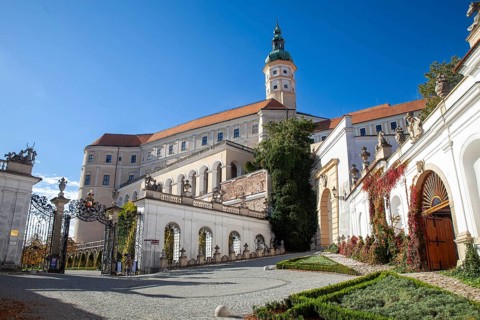A magnificent castle with a richly decorated entrance gate, surrounded by trees under a blue sky,