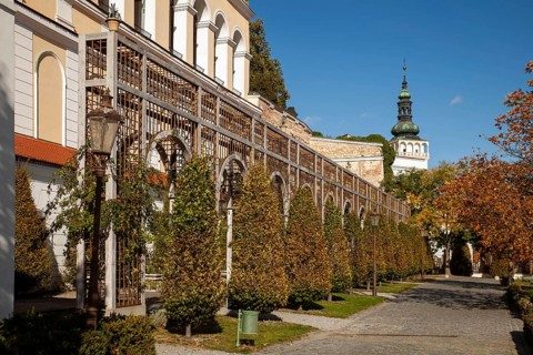 A well-tended garden with trees and antique lanterns in front of a series of arches, Mikulov