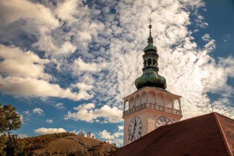 A church tower with a clock sits enthroned against a cloudy sky and overlooks a hill, Mikulov