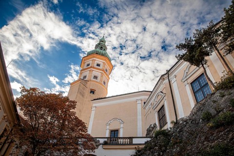 A striking tower stands out against a cloudy sky, next to it an autumn-coloured tree, Mikulov