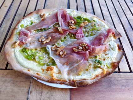 Close-up of a pizza tarte flambée with raw ham and walnuts, crispy base, served to a high standard,