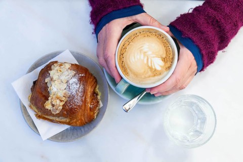 Warm cappuccino with an almond biscuit on a table, hands warming the cup, Lower Austria Austria