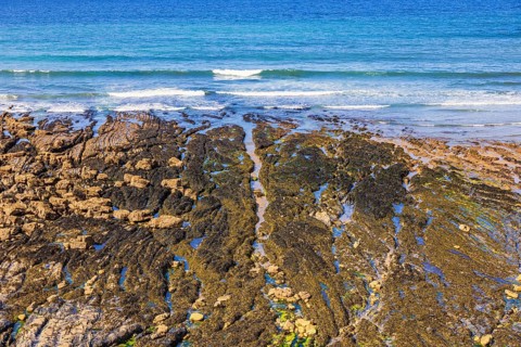 Beach by the sea at low tide with water pools and waves crashing on the shoreline a sunny summer