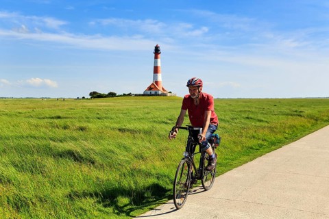 Cyclist, cycle tour through salt marshes, Westerheversand lighthouse on the horizon, Cirrus,