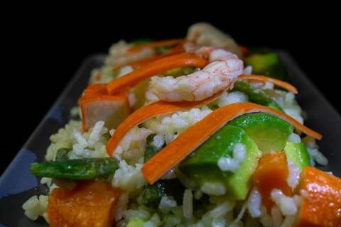 Rice salad with shrimp, red bell pepper and avocado, on black background