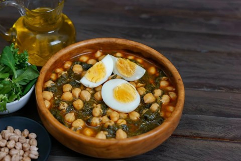 Wooden bowl with chickpeas with spinach and hard-boiled egg on wooden table