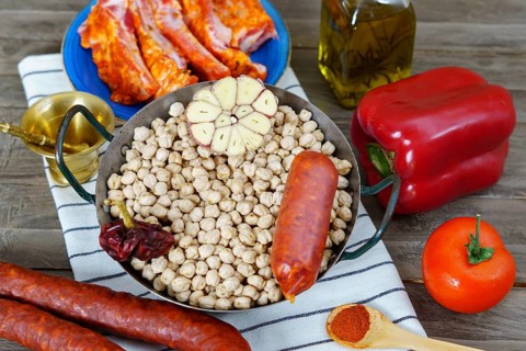 Raw chickpeas in a casserole with the ingredients to make the stew