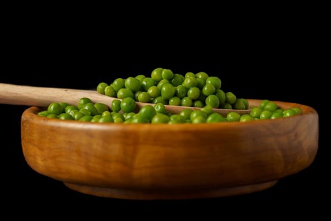 Wooden bowl with fresh peas and wooden spoon isolated on black background