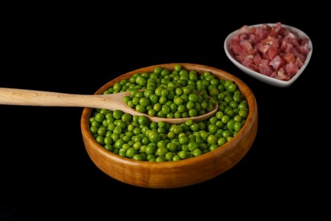 Wooden bowl with peas and white bowl with iberian ham isolated on black background