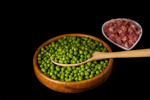 Wooden bowl with peas and white bowl with iberian ham isolated on black background