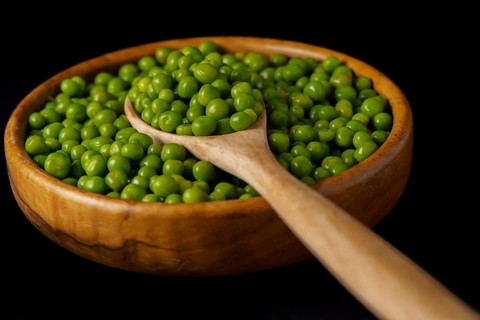 Wooden bowl with fresh peas and wooden spoon isolated on black background