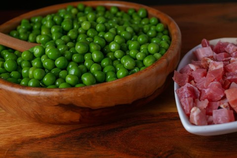 Wooden bowl with peas and white bowl with iberian ham isolated on black background