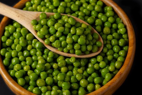 Wooden bowl with fresh peas and wooden spoon isolated on black background