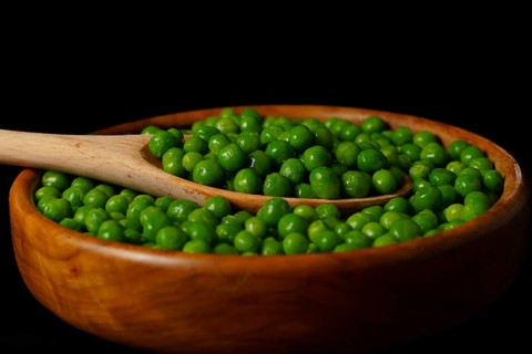 Wooden bowl with fresh peas and wooden spoon isolated on black background