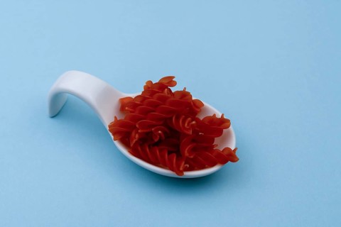 White ceramic spoon with red spiral macaroni and blue background