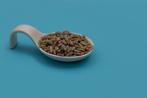 White ceramic spoon with peeled sunflower seeds and blue background